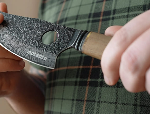 Hand holding the Matsato Osuren knife with the index finger through the finger hole in the blade