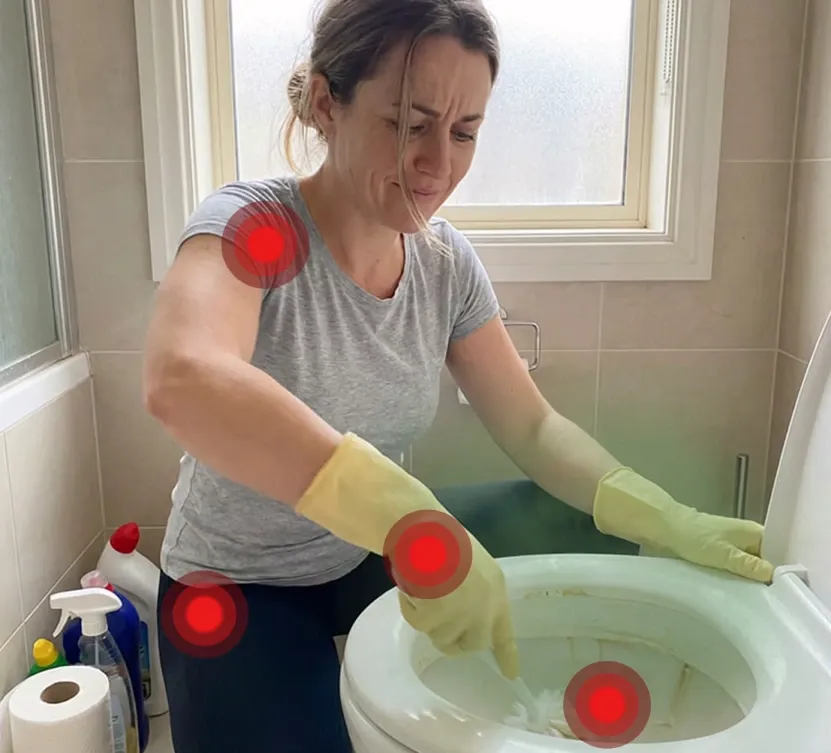 Person pÄ knÊ pÄ badevÊrelsesgulvet, der skrubber en toiletkumme i hÄnden med handsker og bÞrste