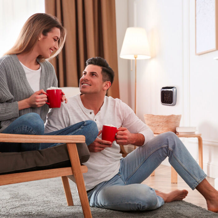 Stel ontspant op de bank in een woonkamer met de WellHeater-stopcontactkachel op de achtergrond aan de muur
